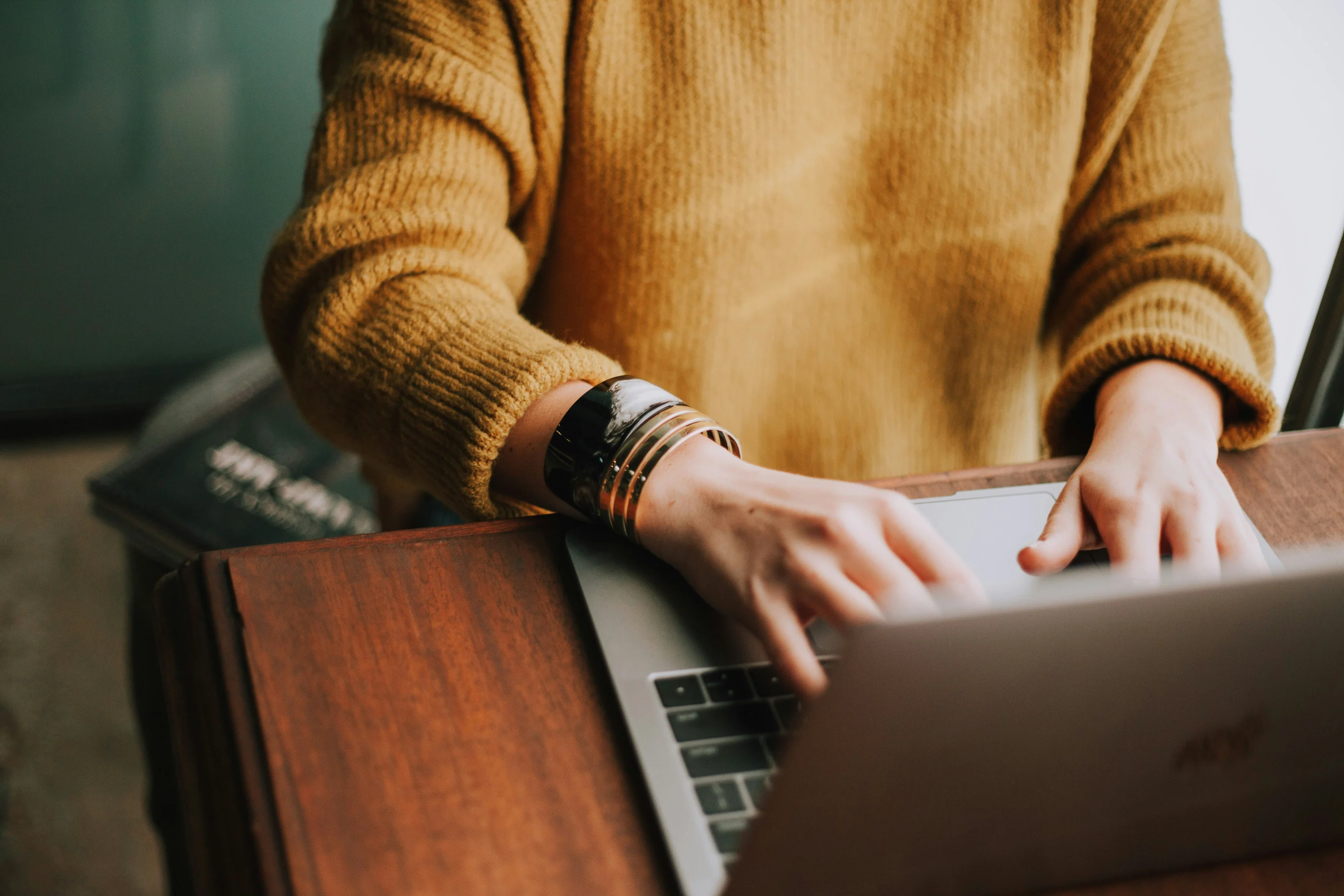 Person typing with both hands on a laptop with a yellow sweater on