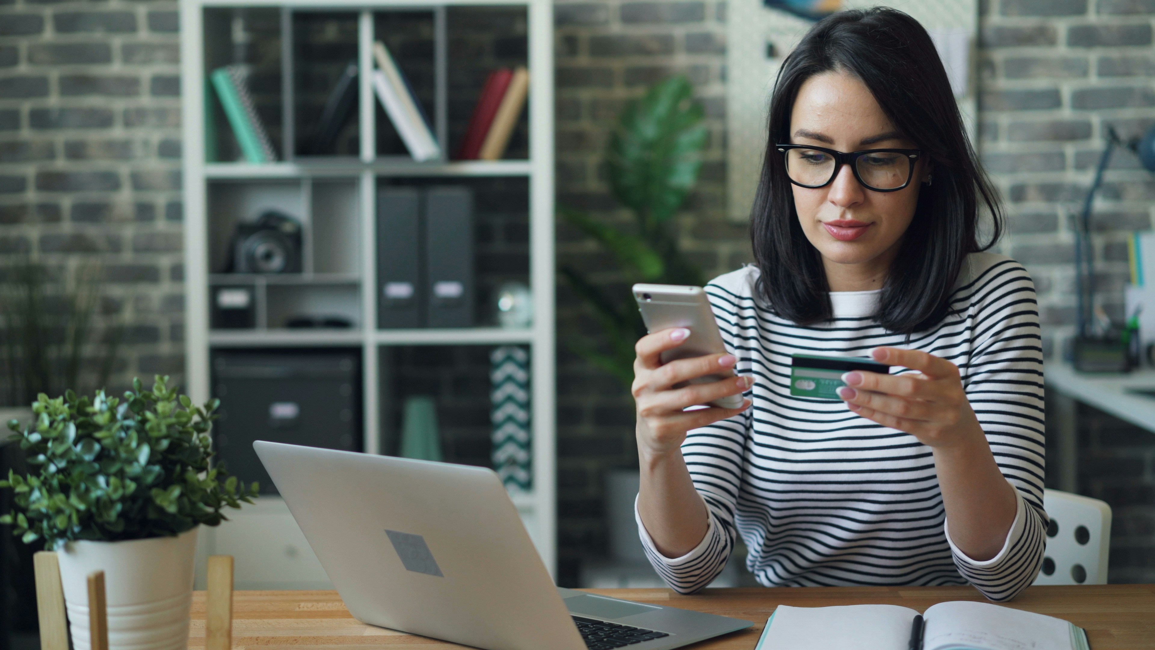 woman reviewing her debit card sitting by computer